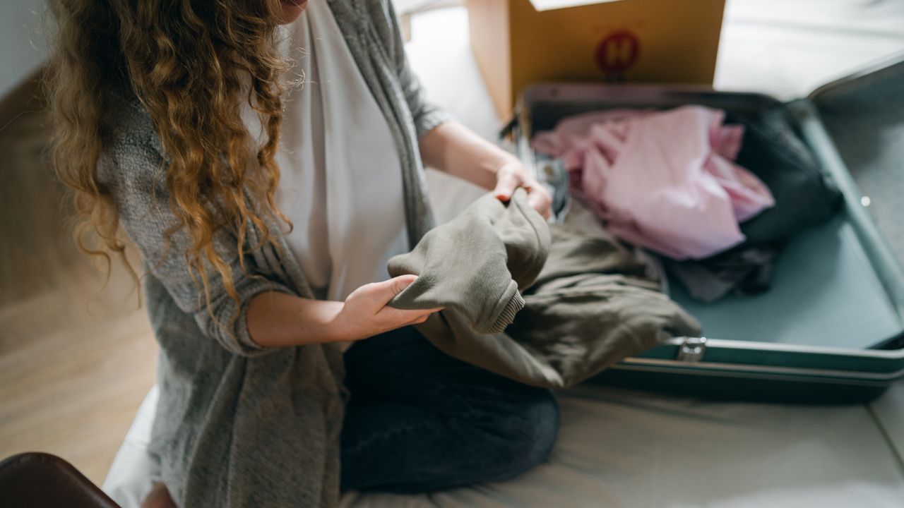 Folded clothes being sorted over an open suitcase before a trip